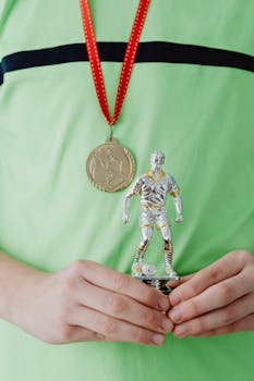 Close-up of hands holding a soccer trophy with a gold medal around neck.