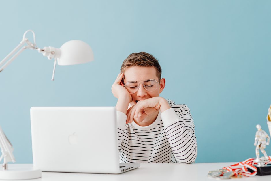 Young man in glasses yawning at desk with laptop and lamp, looking tired. Young man in glasses yawning at desk with laptop and lamp, looking tired.
