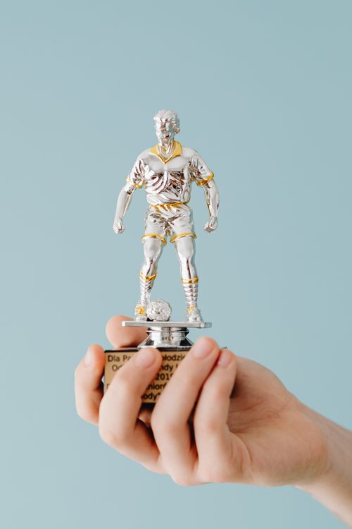 Free Close-up of a hand holding a silver soccer trophy against a light blue background. Stock Photo