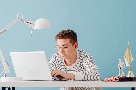 Teenager focused on laptop work in a modern, minimalist home office setting.