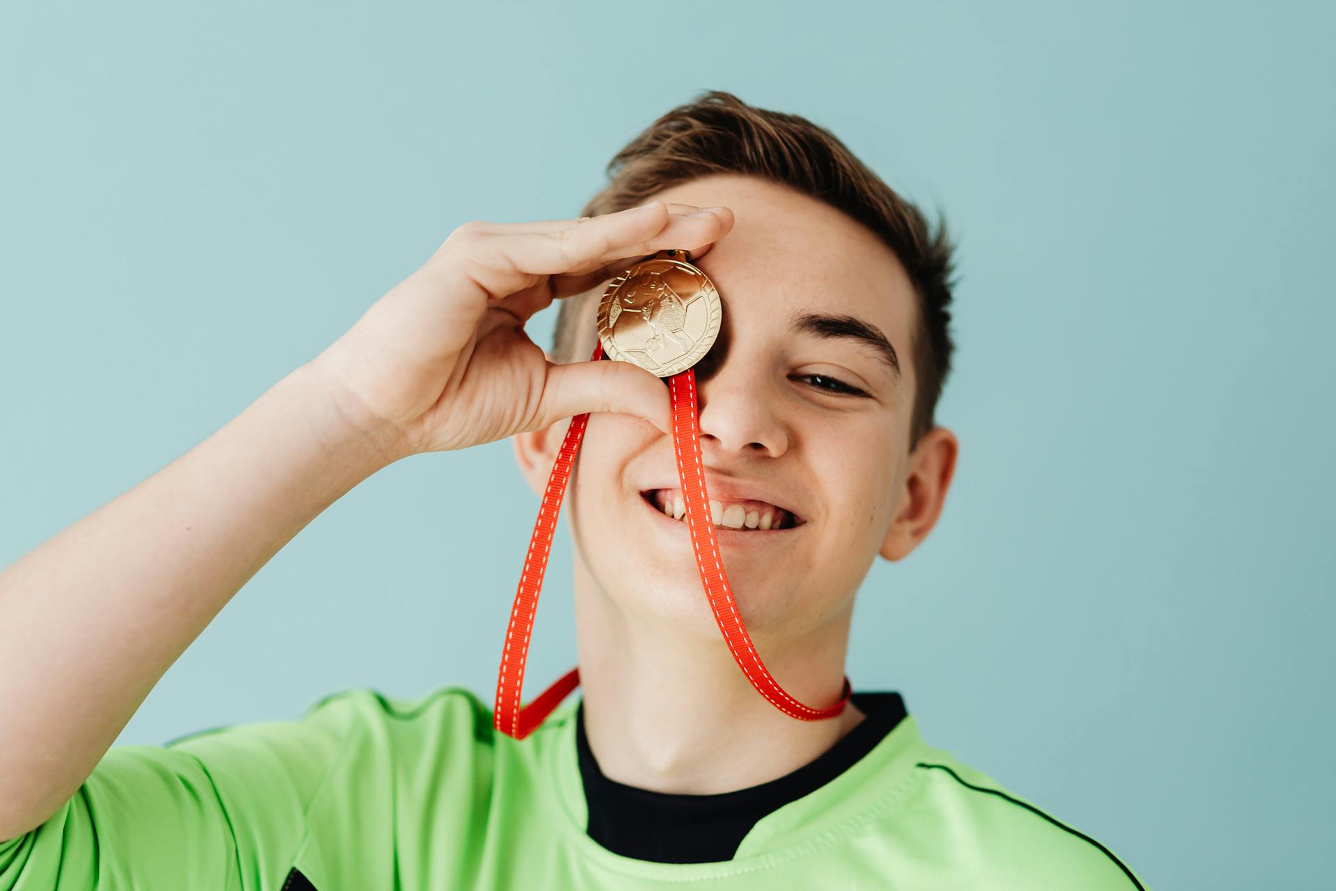 Un adolescent tient une médaille devant son œil et sourit