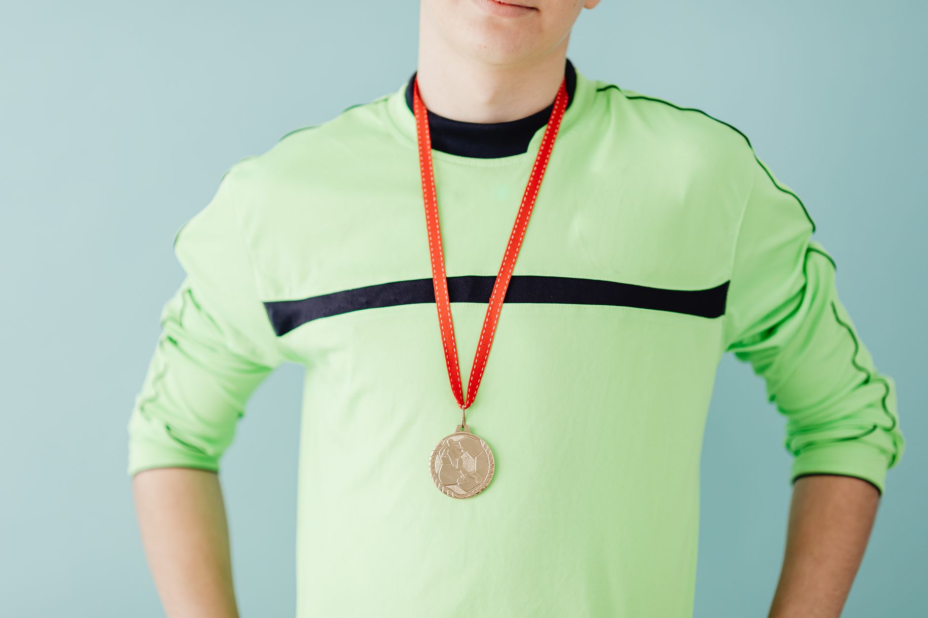 Teenager in sportswear proudly wears a gold medal with a confident pose, set against a blue backgrou