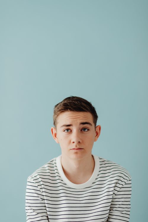 Free Minimalist portrait of a young boy wearing stripes with a blue background. Stock Photo