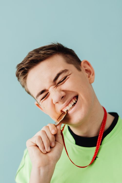 Free Joyful teen biting a gold medal on a light background, expressing success. Stock Photo