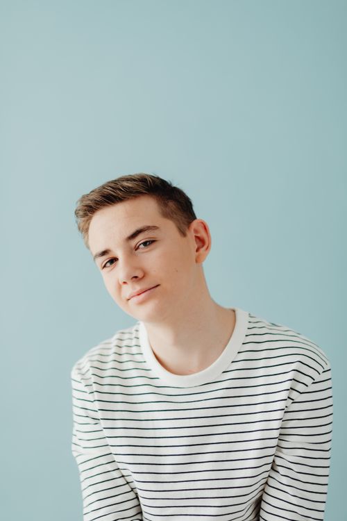 Free A cheerful teenage boy poses casually in a striped blouse against a pastel background. Stock Photo