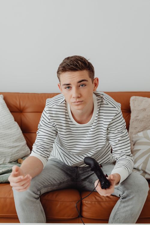 Free Teenager with a game controller sitting on a sofa indoors. Stock Photo