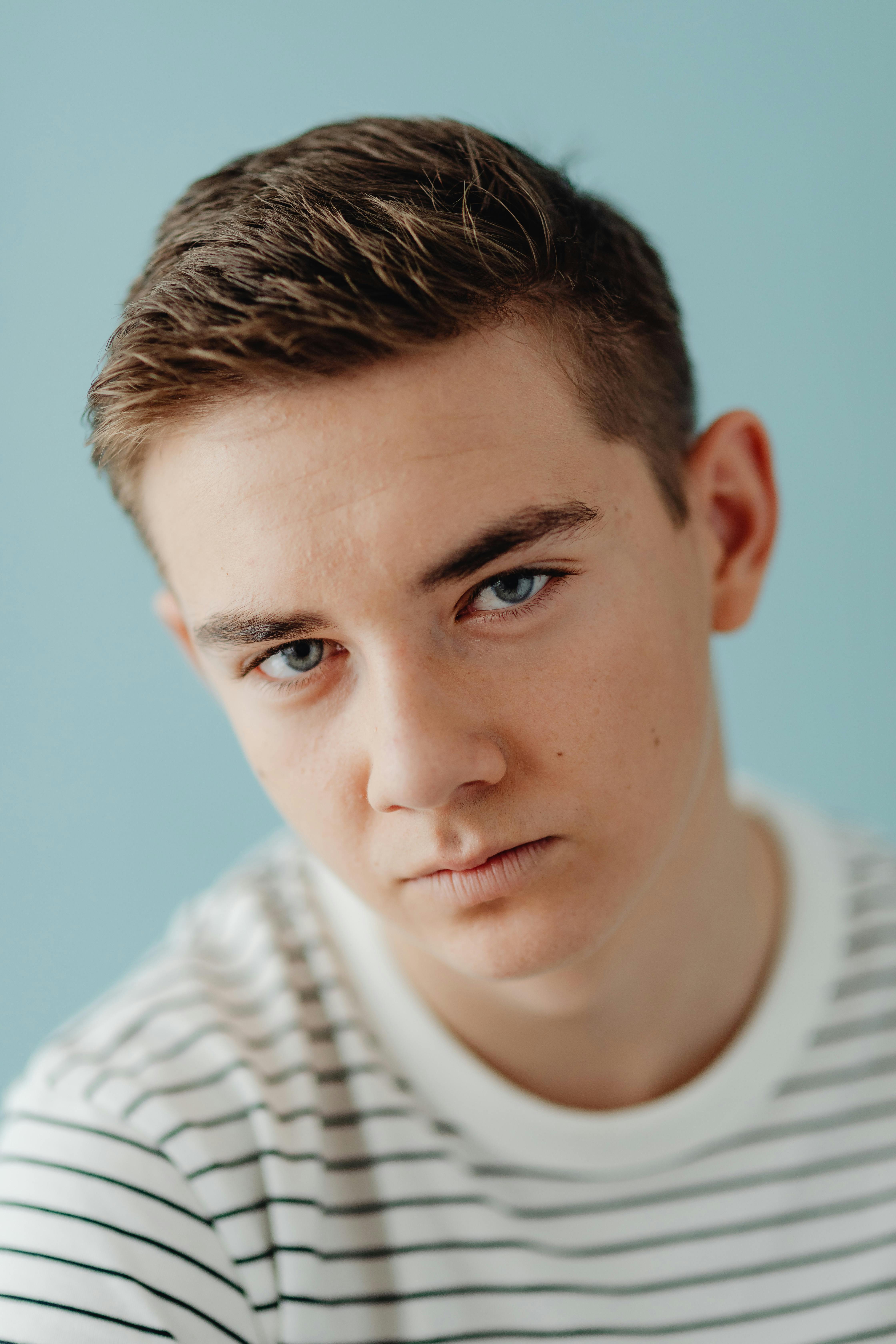 A thoughtful teenage boy with blue eyes in a studio portrait with a blue background.