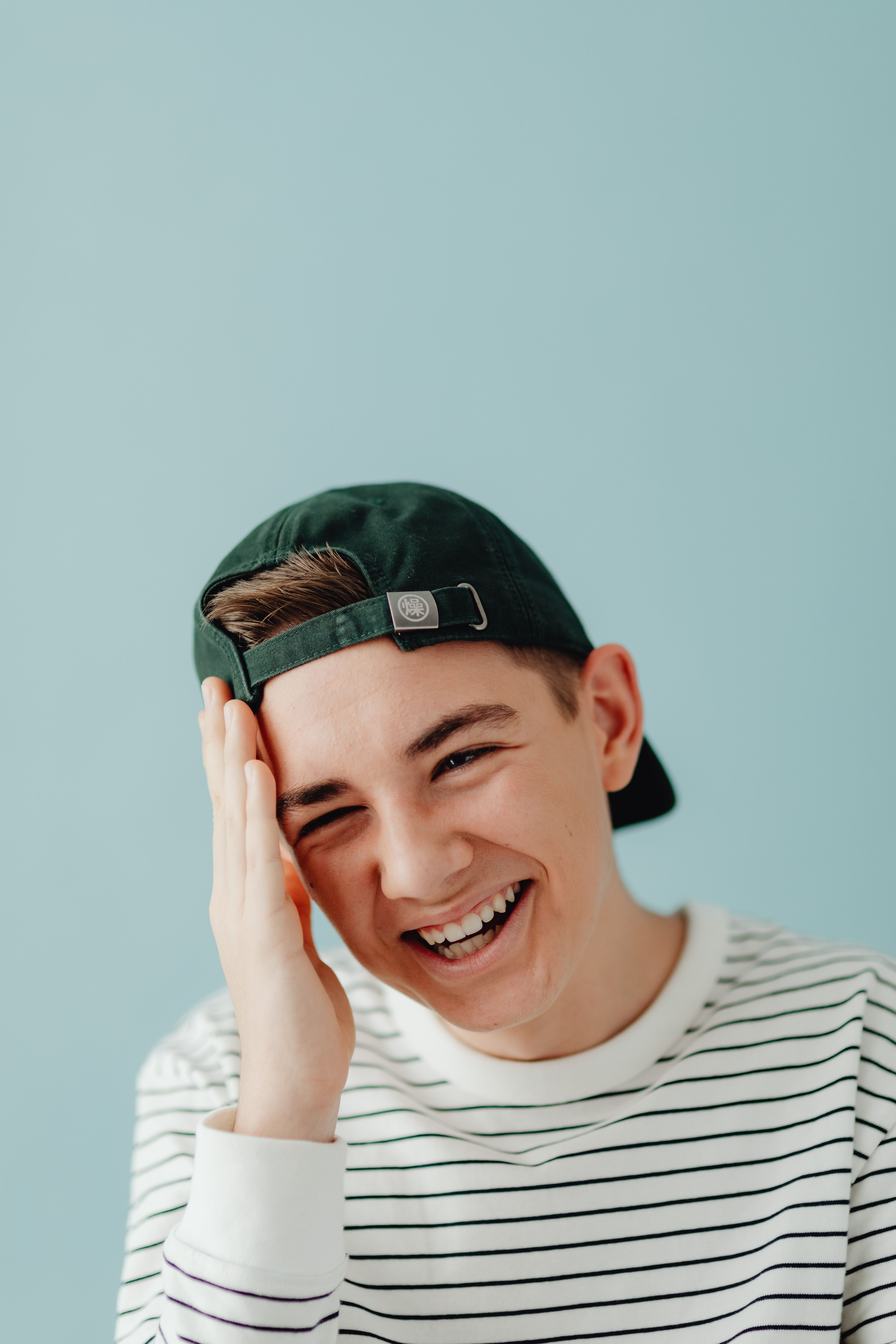Teen boy in a casual striped sweater laughing playfully against a blue backdrop.