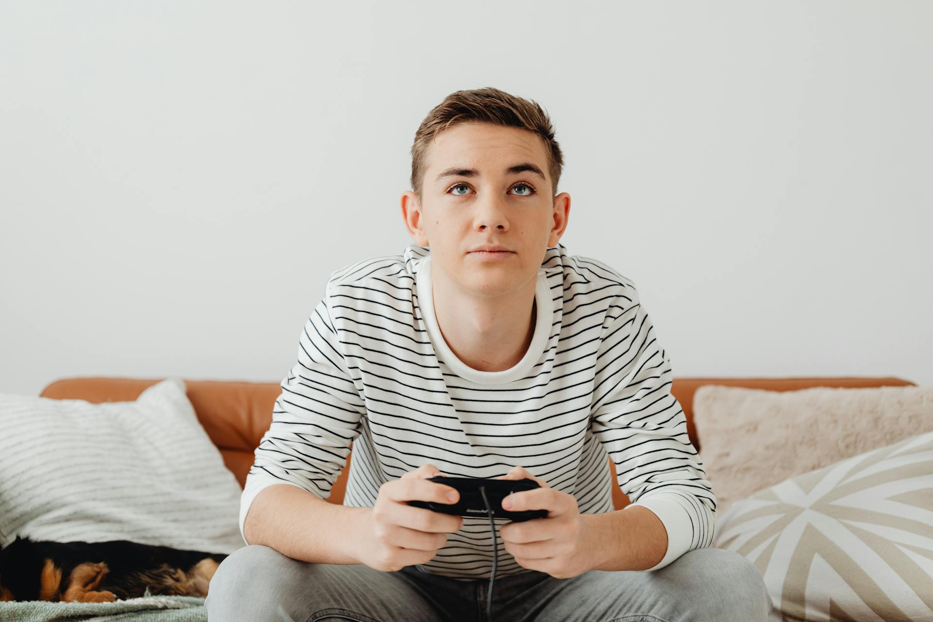 Teenage boy sitting on couch playing video game with console controller.