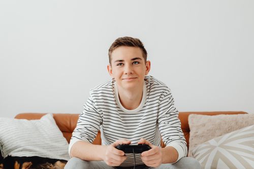 Free Smiling teen playing video games on a couch at home, enjoying leisure time. Stock Photo