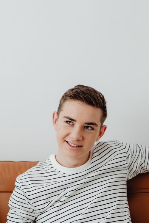 Free Portrait of a smiling young man in a striped shirt relaxing on a couch at home. Stock Photo