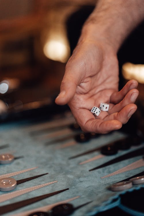 Crop unrecognizable male with dice playing entertaining board game backgammon at spare time