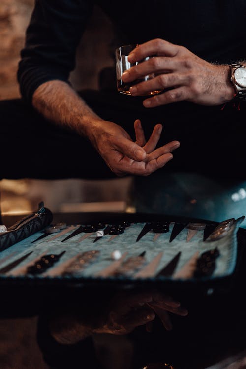 Crop man having whiskey while playing backgammon
