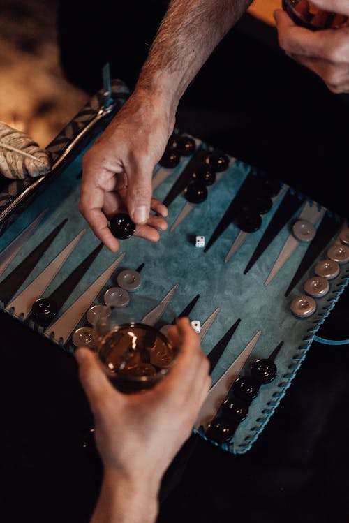 High angle of crop unrecognizable mates with glasses of alcohol playing board game while spending time together