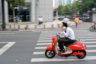 Man in White Long Sleeve Shirt Riding Red Motor Scooter on Road