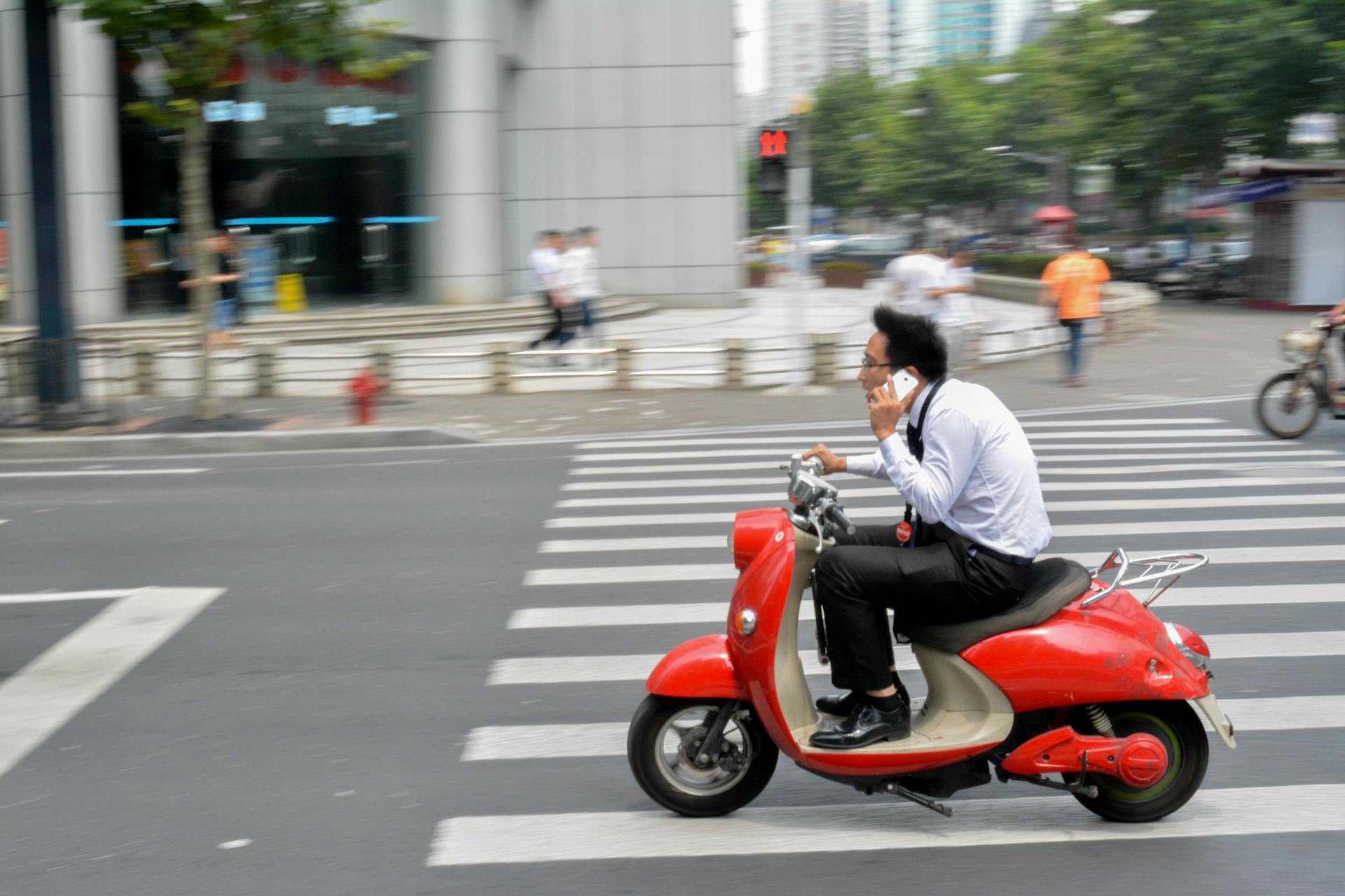 Businessman riding a red scooter while talking on the phone in Shanghai, China.