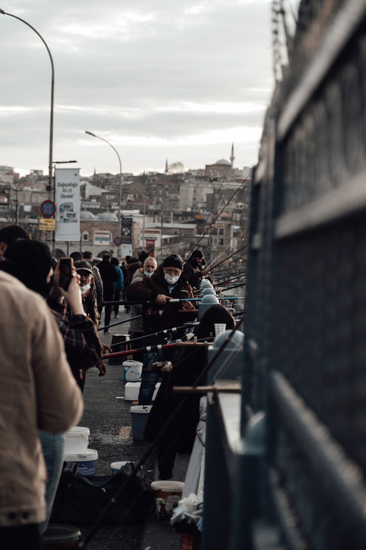 People In Masks Catching Fish And Taking Photo On Bridge