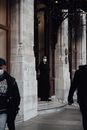 Full body of doorman in protective mask standing near door of aged stone building of hotel