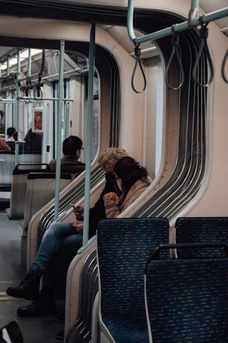 Side view of friends in protective masks sharing mobile phone while riding in metro during pandemic