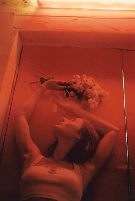 Woman holding flowers above head in a dramatic red lighting, creating a romantic and moody atmosphere.