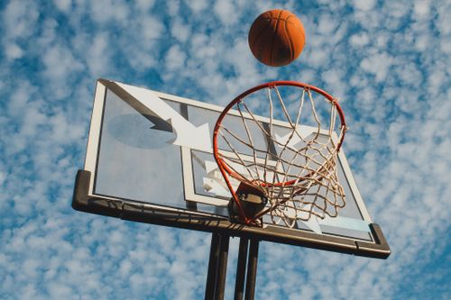 Free Basketball nearing the hoop with a cloudy sky backdrop, captured from a low angle. Stock Photo