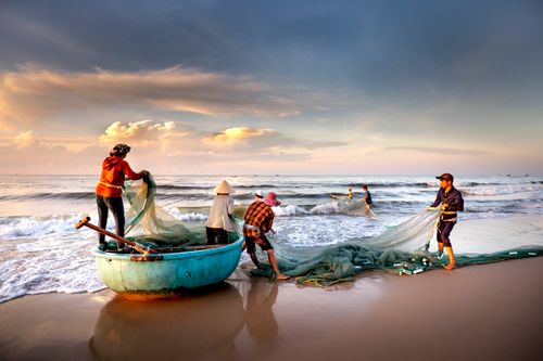 Free Traditional fishermen repairing nets by the sea in La Gi, Vietnam at sunrise. Stock Photo