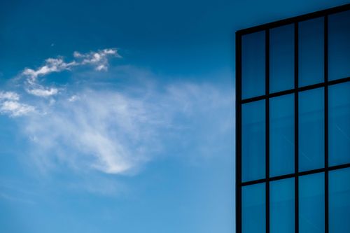 Free Low angle fragment of minimalist exterior of contemporary building with glass walls reflecting blue sky in sunlight Stock Photo
