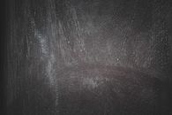 Smeared white paint marks on rough dark surface with stains as abstract background