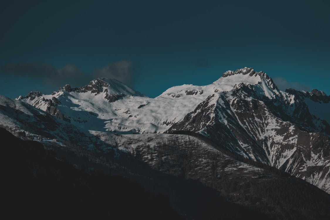 Majestic scenery of huge rocky mountains covered with snow under cloudless evening sky in winter