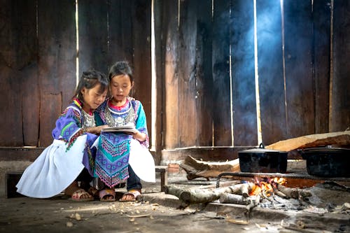 Adorable Kids looking at a Book sitting beside a Fireplace