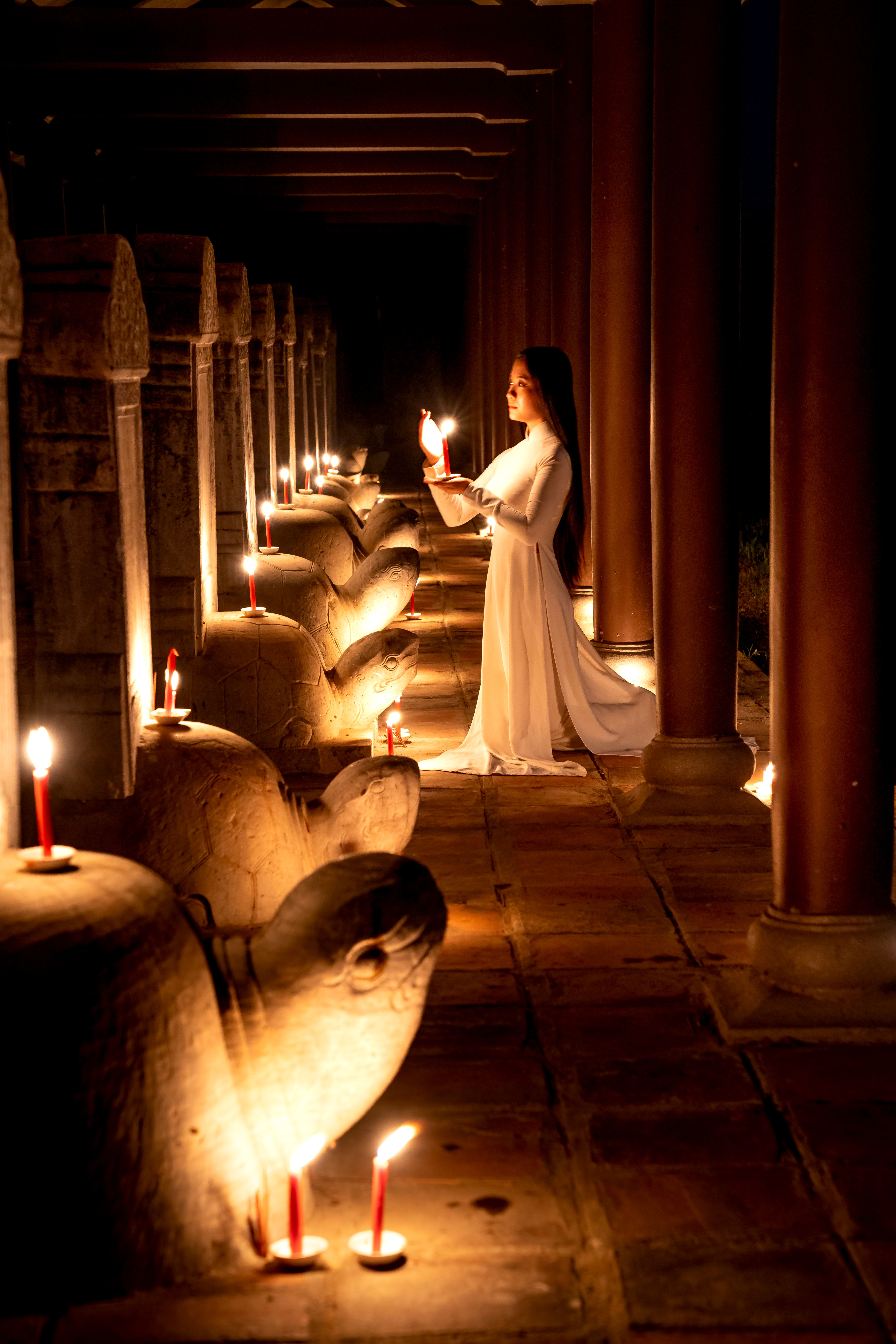 Elegant Vietnamese woman in ao dai lights candles in historic Hue temple at night.