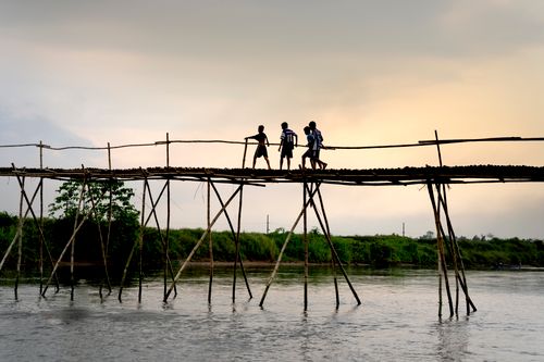 Free Three children walking over a rustic wooden bridge at sunset in Hue, Vietnam. Stock Photo
