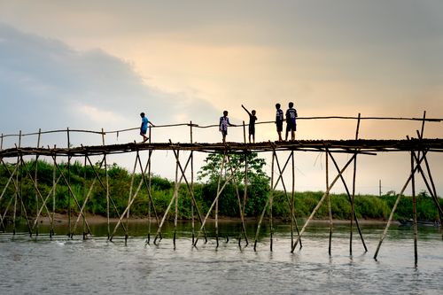 Free Group of children silhouetted on a rustic wooden bridge over a river at sunset in Vietnam. Stock Photo