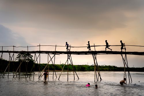 Free Silhouetted children run across a wooden bridge over a river at sunset in Hue, Vietnam. Stock Photo