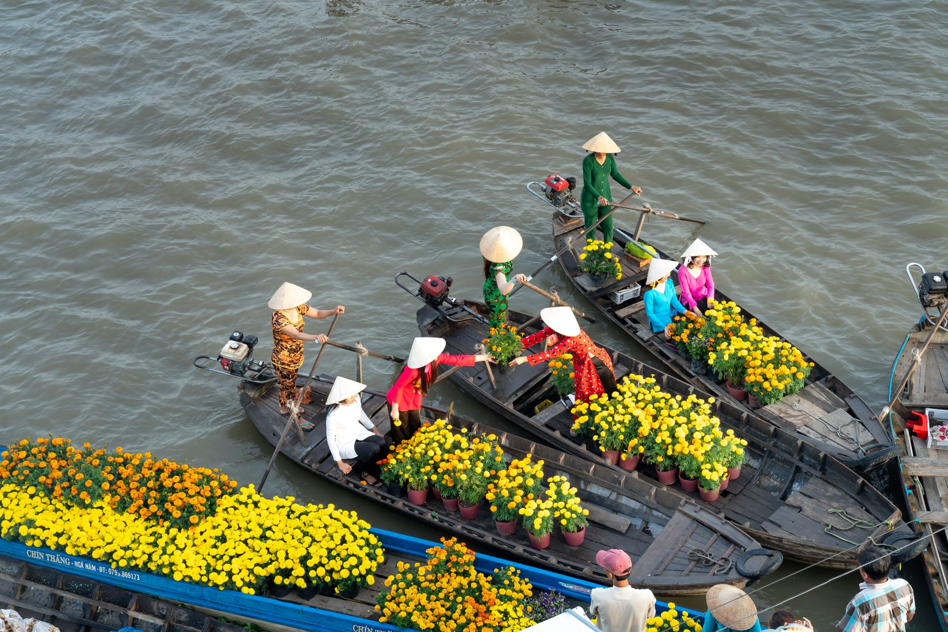 Women selling flowers from rowboats at a vibrant floating market in Soc Trang, Vietnam.