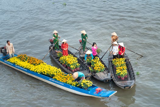 Women in traditional attire selling flowers on boats at a Vietnamese floating market.