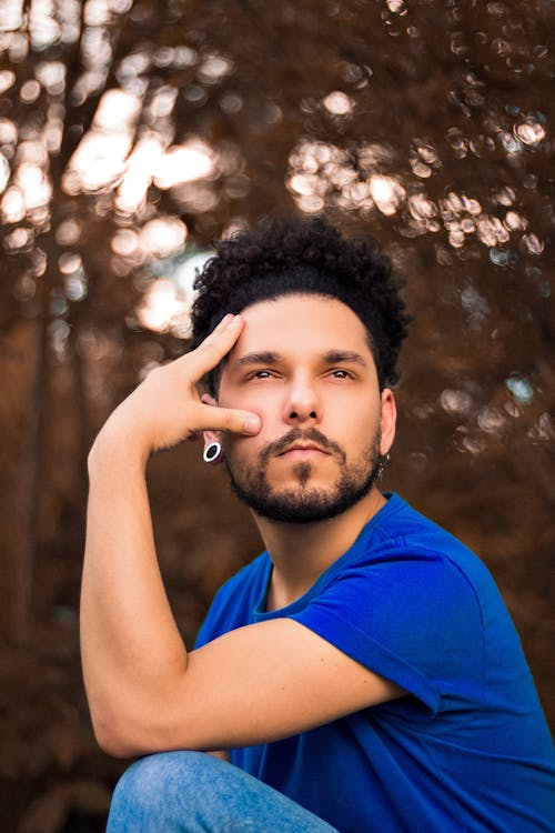 Thoughtful young bearded male in casual outfit with gauged ears touching face and looking away