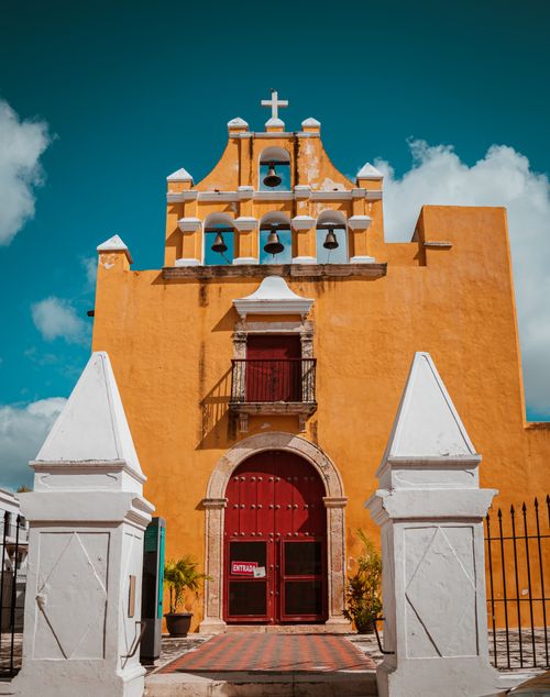 Free Vibrant yellow colonial church facade with red doors and bell towers under a clear sky. Stock Photo