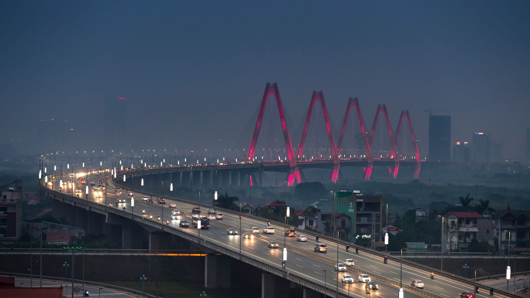 Dramatic aerial view of Hanoi's Nhat Tan Bridge at night, glowing with lights.