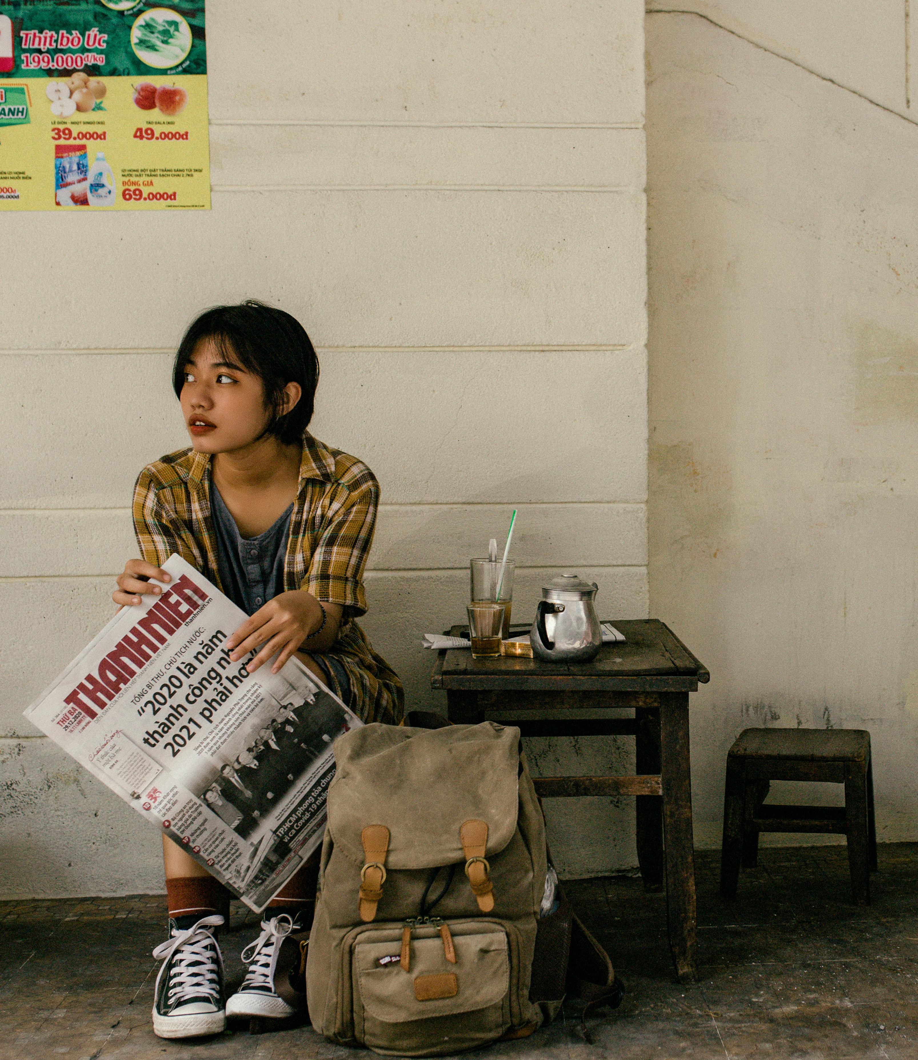 ethnic female traveler with backpack and newspaper near wall