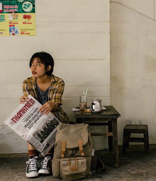 Free Ethnic female traveler with backpack and newspaper near wall Stock Photo