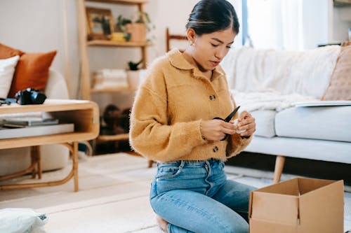 Young woman in trendy outfit with scissors preparing parcel