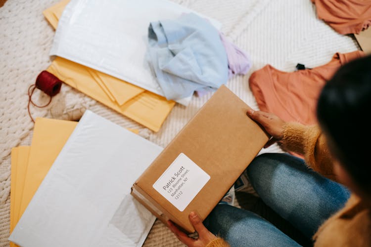 Woman Unpacking Parcel With Address Among Envelopes And Clothes