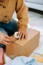 From above of crop anonymous female preparing parcel in carton box on floor among clothes