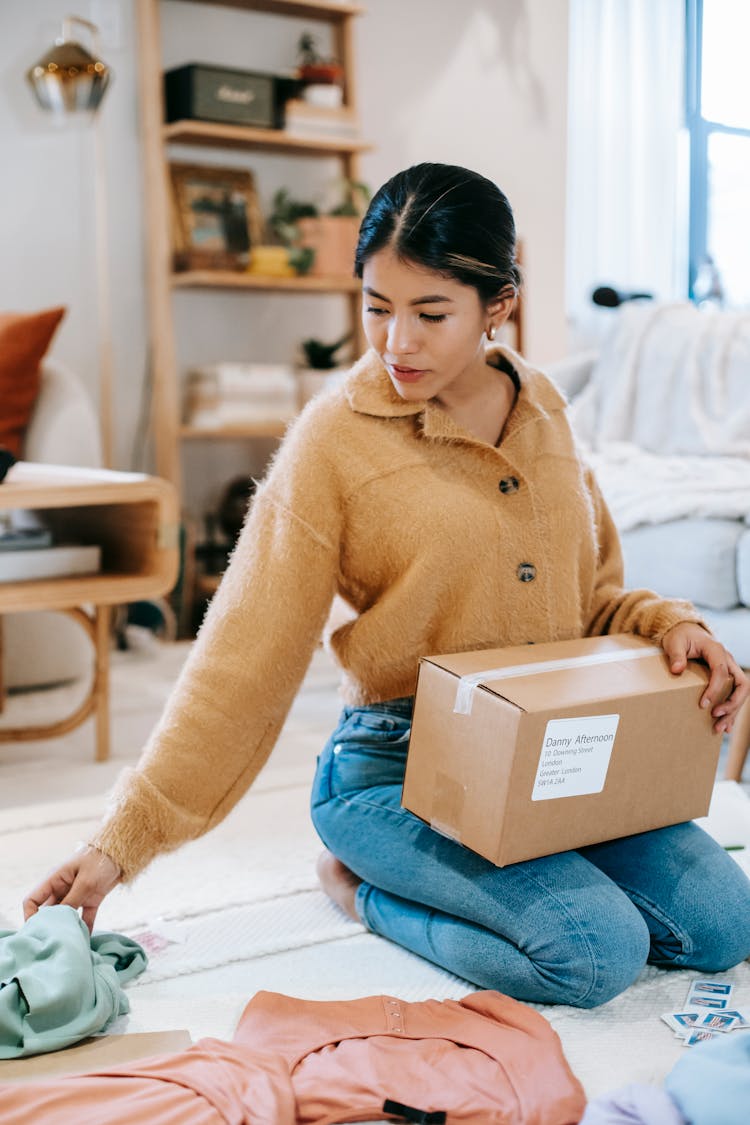 Woman Preparing Box With Parcel Among Clothes