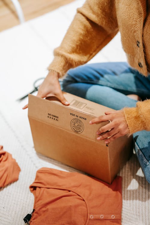 Free From above of crop anonymous female opening carton box with cotton clothes on floor Stock Photo