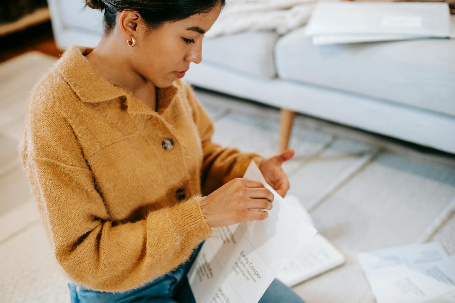 Young woman sitting on the floor reviewing paperwork in a cozy home setting.