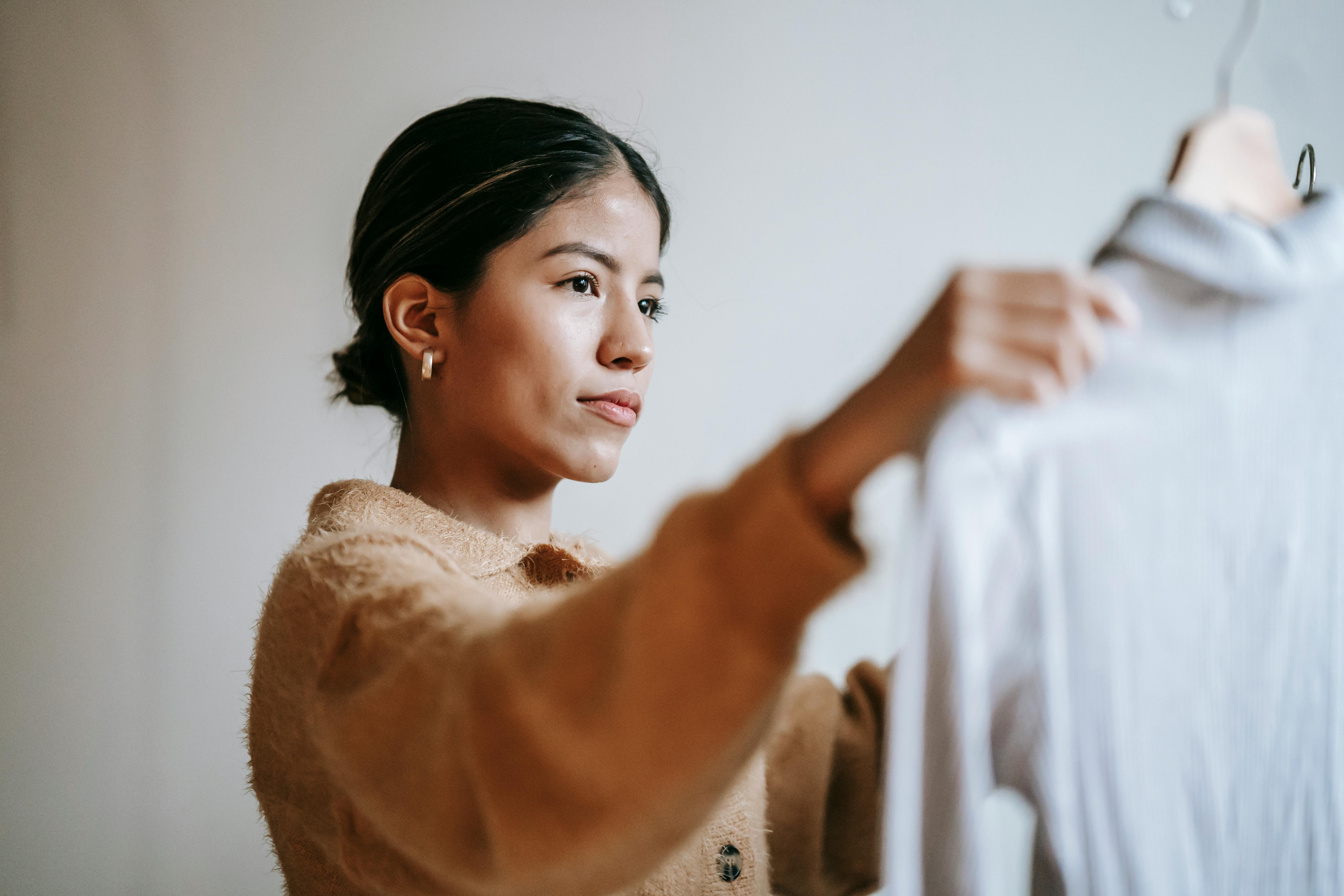 ethnic woman choosing shirt in room