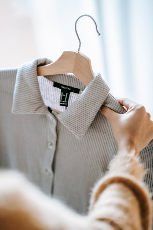 Crop anonymous female designer holding wooden hanger with elegant shirt while preparing for fashion event