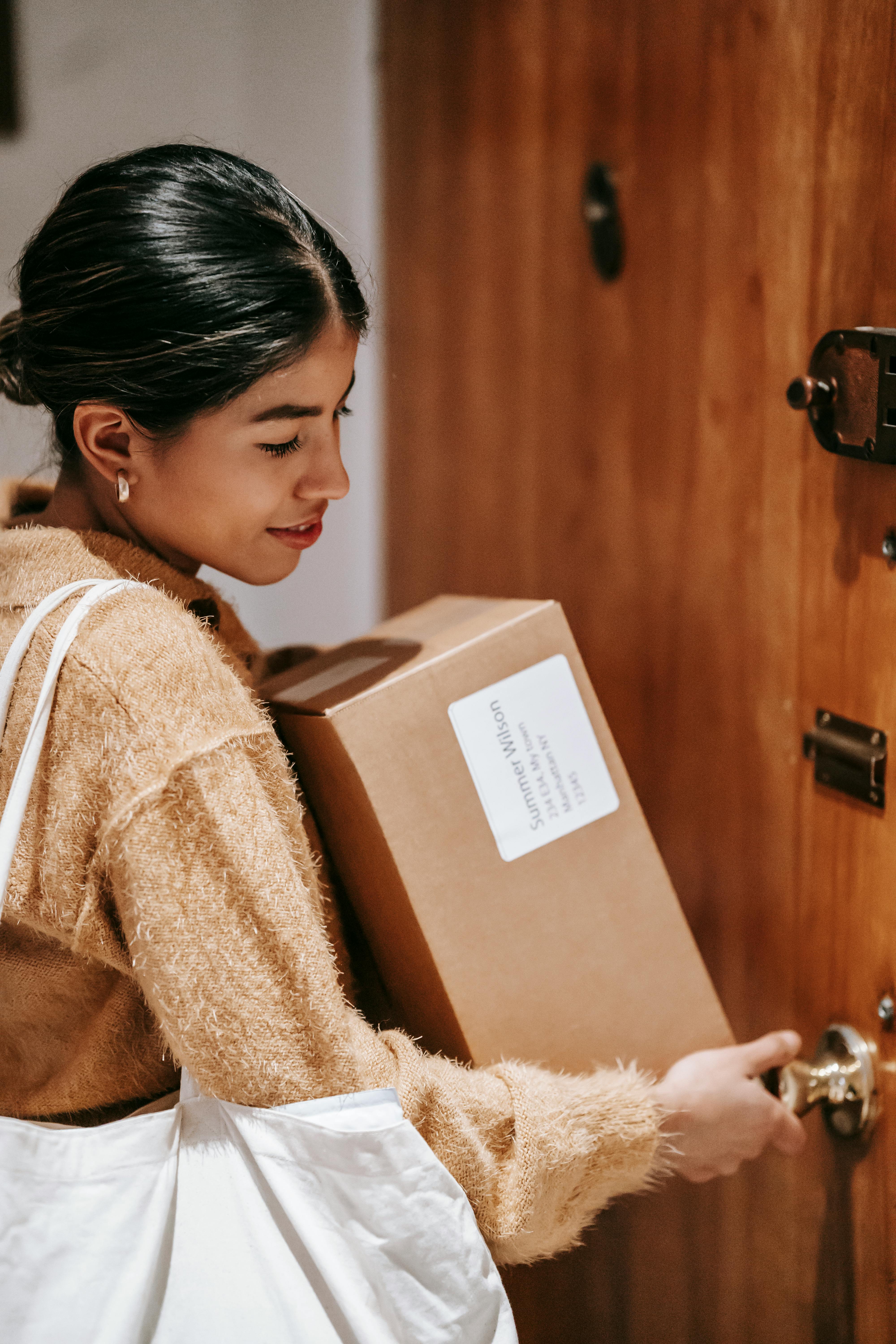 ethnic woman with carton boxes opening door